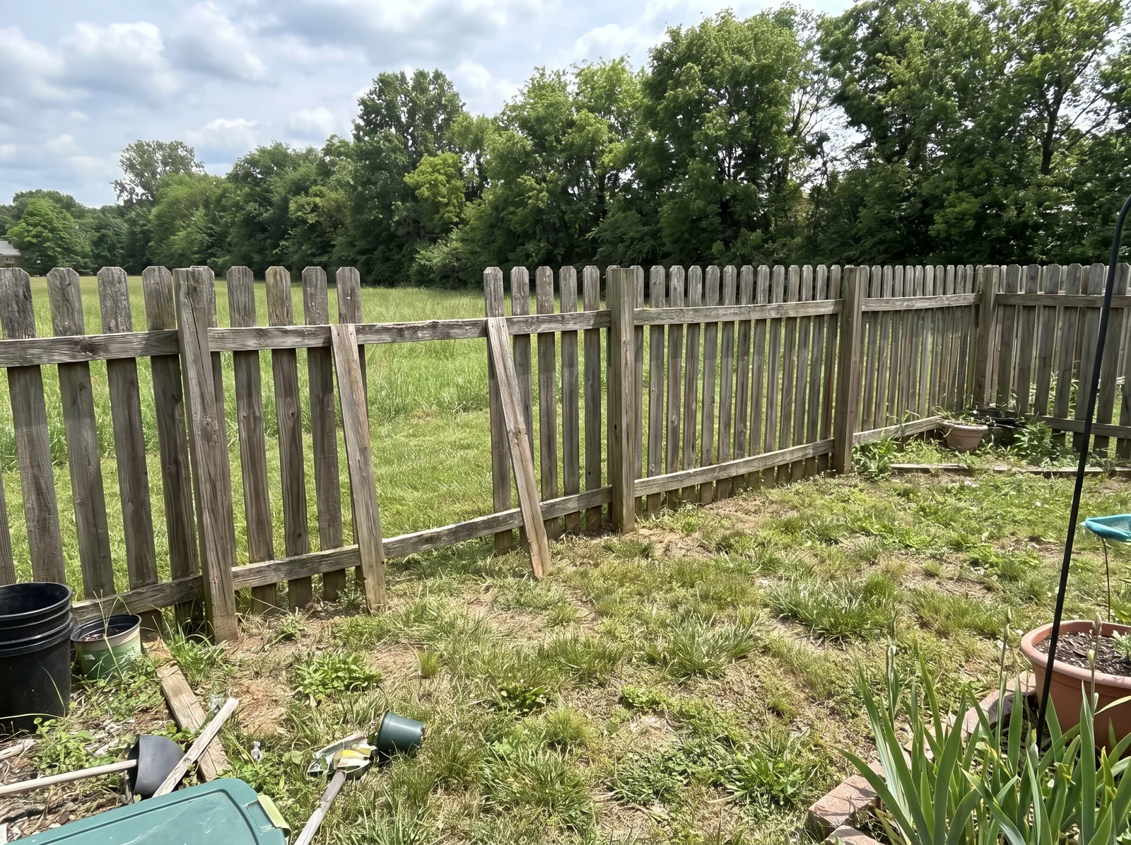 Weathered pressure treated pine picket fence along a rural back property line with a warped, bowed board