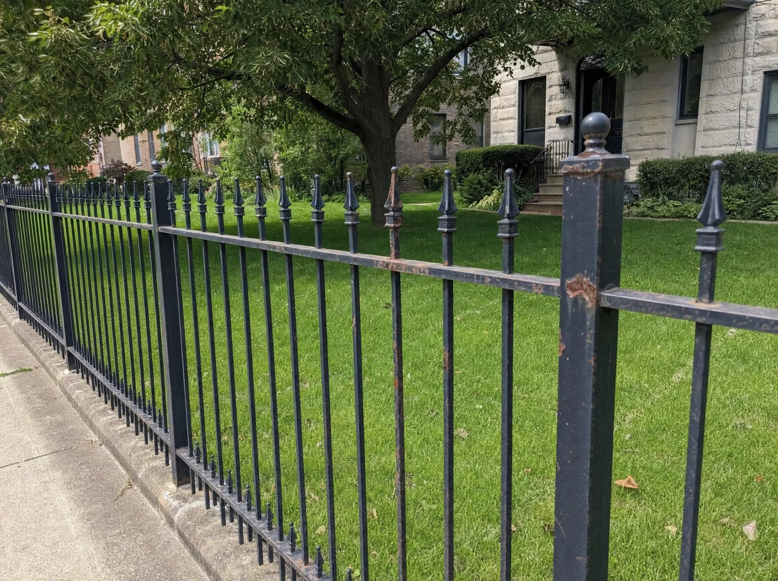 Wrought iron fence along a sidewalk with rust breaking through the coating on a post and pickets