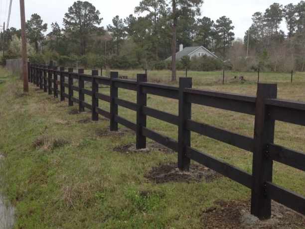 Stained rail fence running the length of an open field