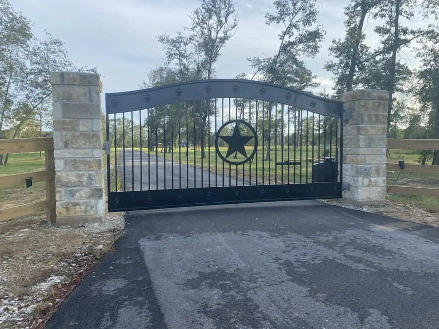 Automatic driveway gate with an operator arm between stone columns