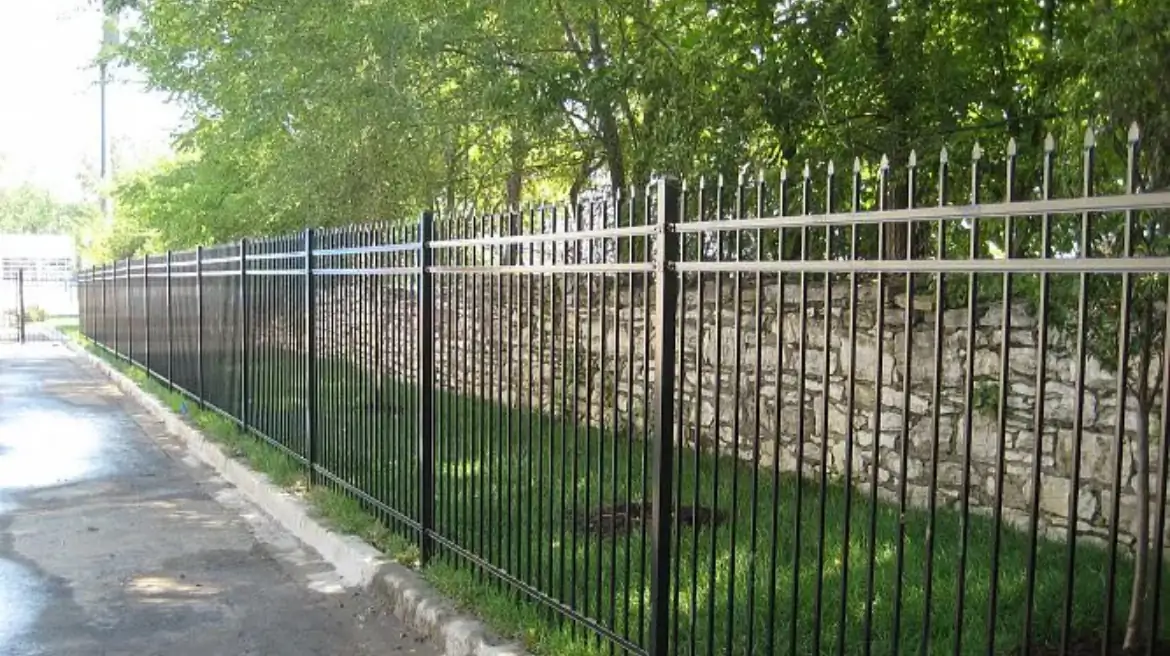 Black aluminum fence panels along a sidewalk above a stone retaining wall