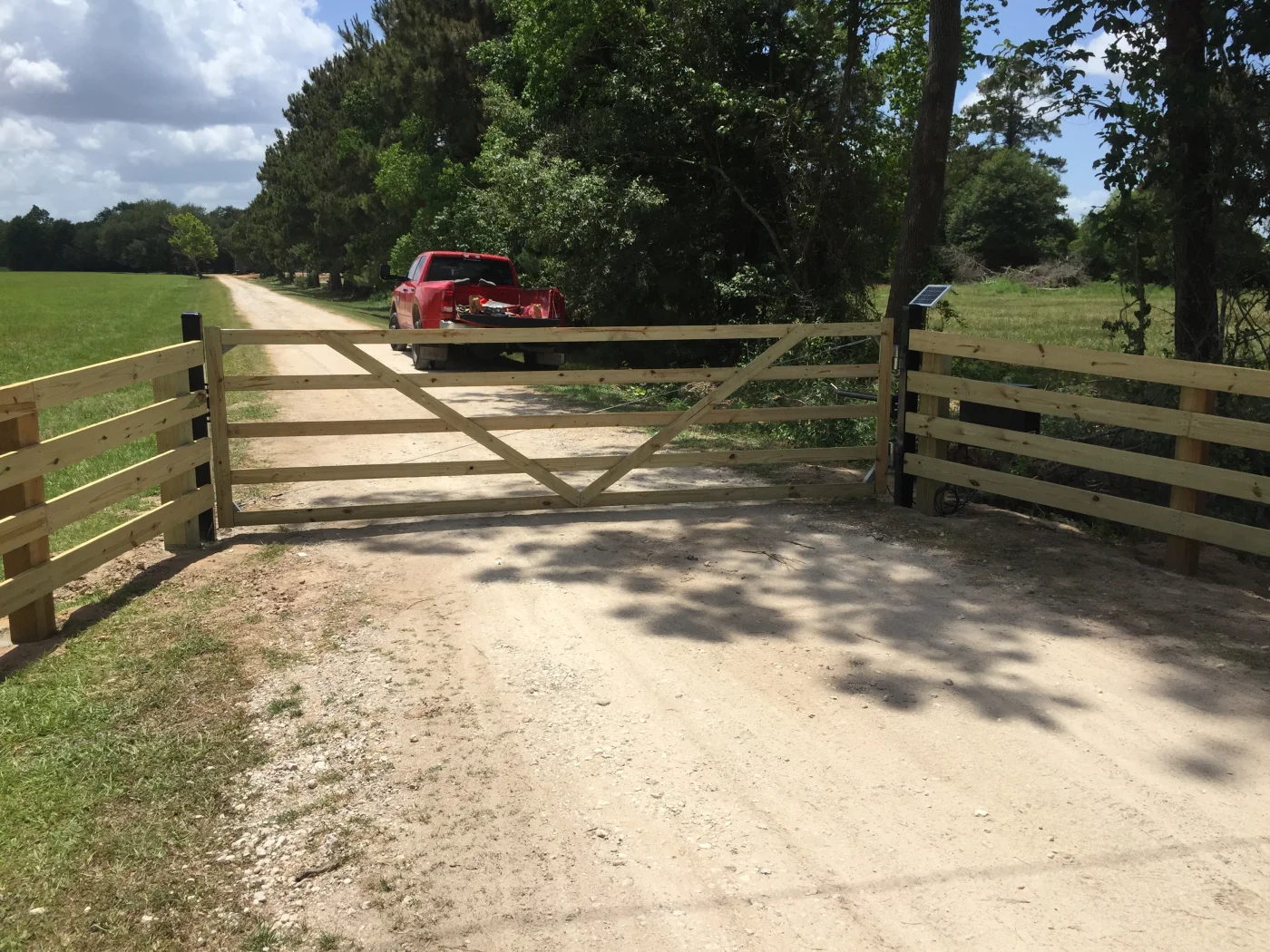 Wood swing driveway gate closed across a gravel entrance