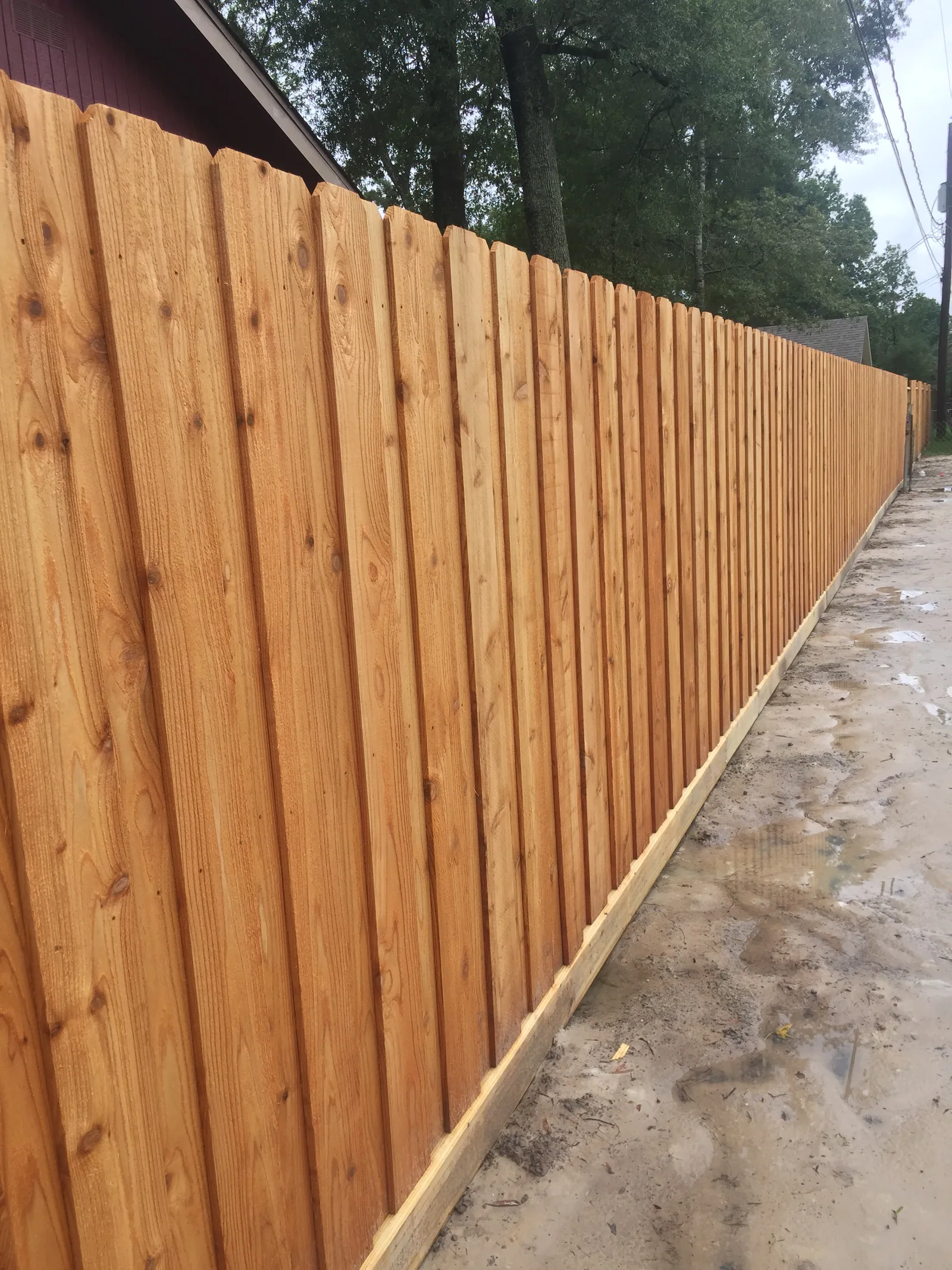 Cedar privacy fence along a wet gravel drive