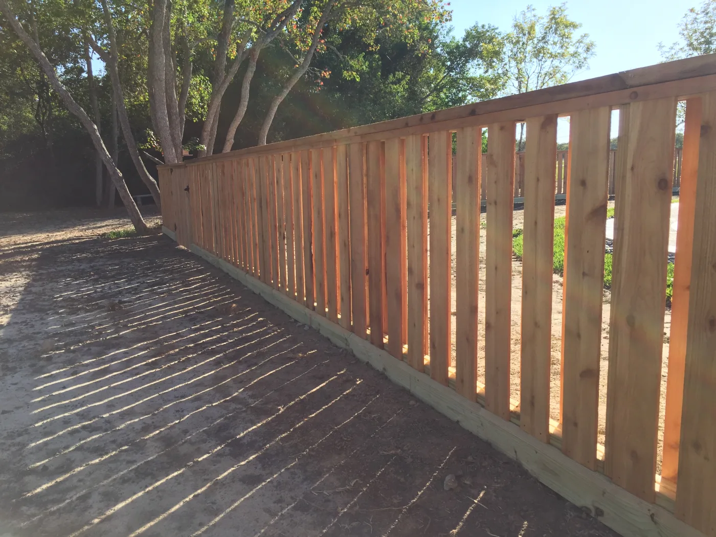 Cedar fence with pickets alternating front and back along a dirt drive